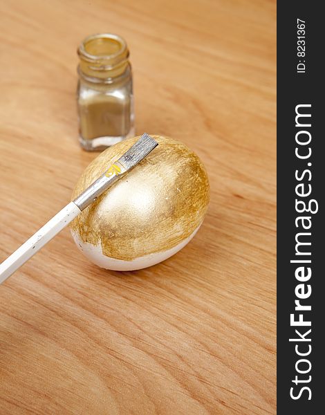 An egg being painted gold with paint and brush. Making a golden egg at home.