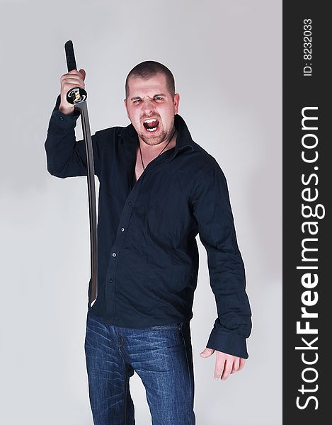 An very angry and dangerous young man wit a long sword screaming at the photographer, with light gray background. An very angry and dangerous young man wit a long sword screaming at the photographer, with light gray background.