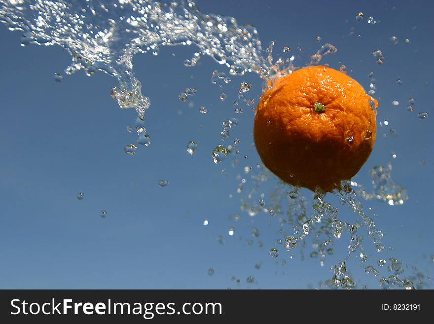 Orange flying through being sprayed by water on a blue sky background. Orange flying through being sprayed by water on a blue sky background.
