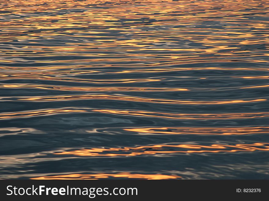 Streaks of gold pass across a water reflection at sunset. Streaks of gold pass across a water reflection at sunset.