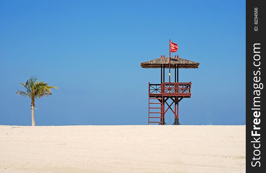 Red flag on the beach. A lifeguards hut ant palm tree. Red flag on the beach. A lifeguards hut ant palm tree.