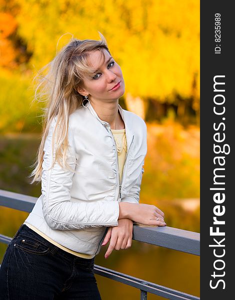 Pretty girl in white jacket near fence with blurry yellow autumn background