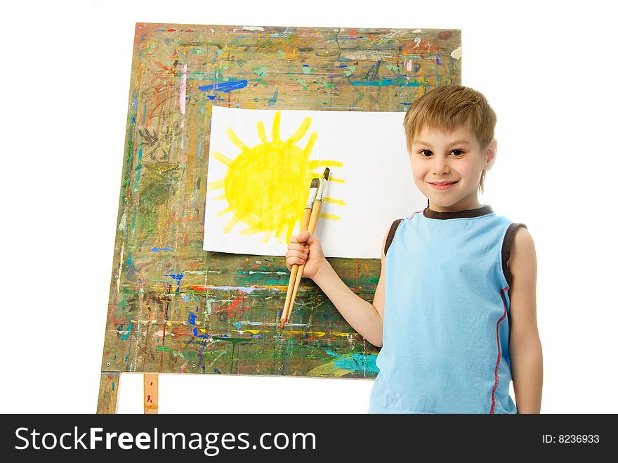 Happy boy standing near the easel with the picture of the Sun he has just painted. Happy boy standing near the easel with the picture of the Sun he has just painted