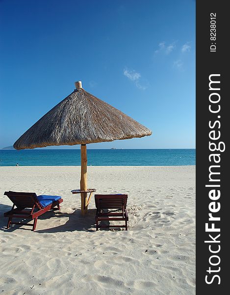 Two beach chairs under a parasol on the white sandy beach at a resort. Two beach chairs under a parasol on the white sandy beach at a resort.