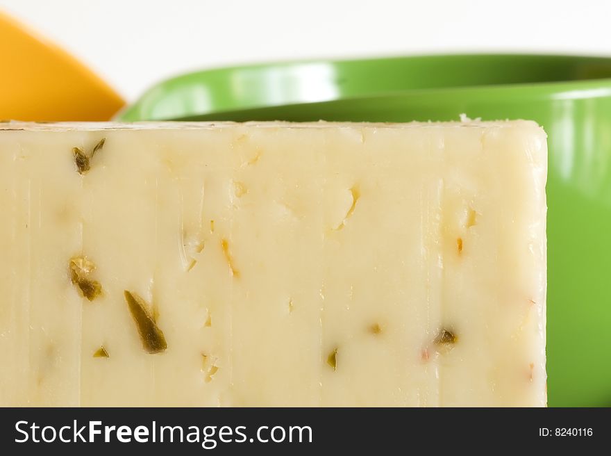 Macro cheese close-up of long rectangular shaped white orange wedge of aged monteray jack and jalepano pepper cheese containing showing the texture of the cheese sitting on black plate against a white wall with the crumbly texture of the aromatic cheese with green cup yellow cup