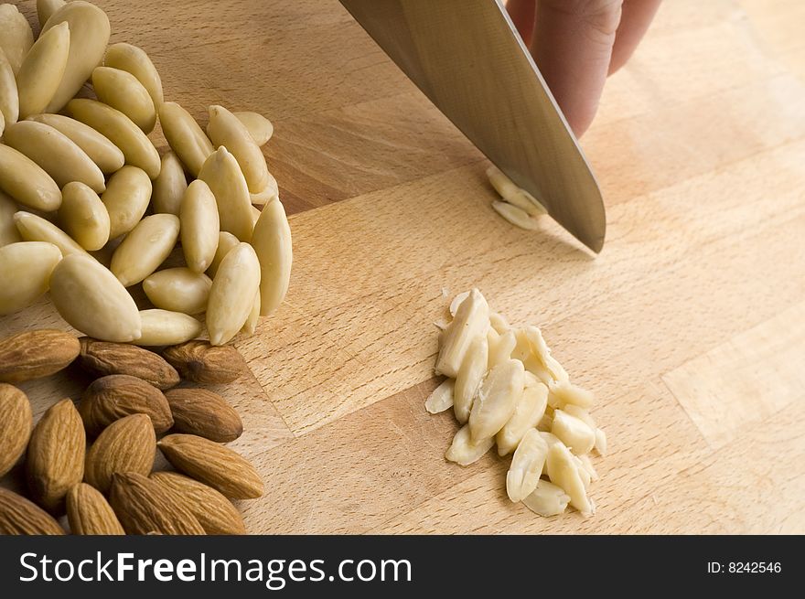 Hand chopping almond alongside pile of natural and peeled almonds on chopping board. Hand chopping almond alongside pile of natural and peeled almonds on chopping board.