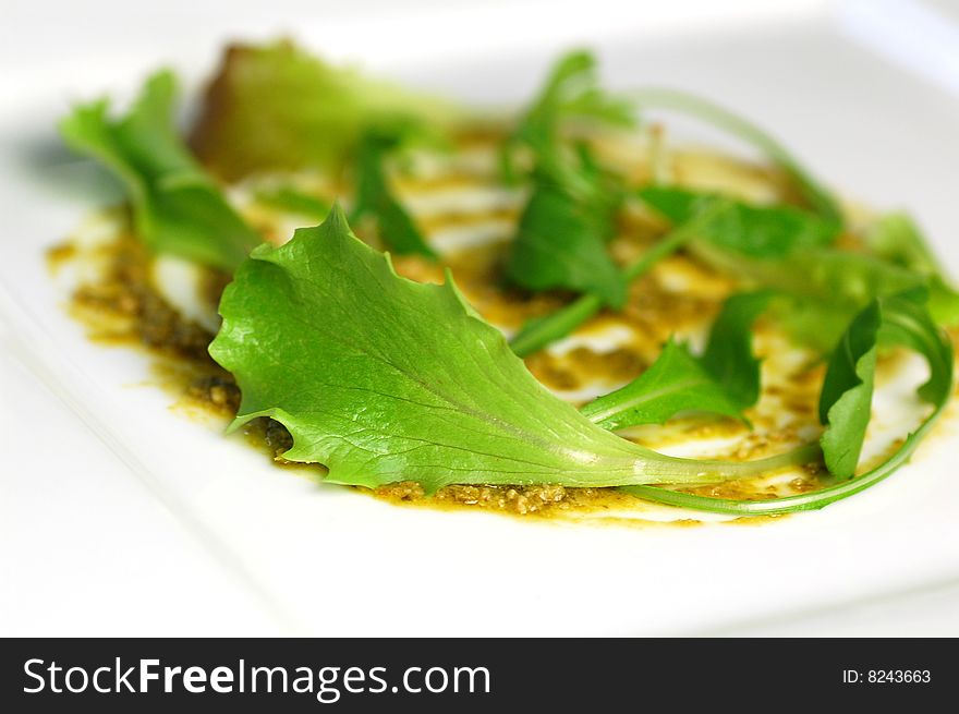 A plate dressed with pesto and salad.