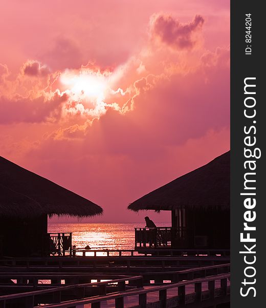 Human silhouette in water bungalow at sunset, abstract vacation background