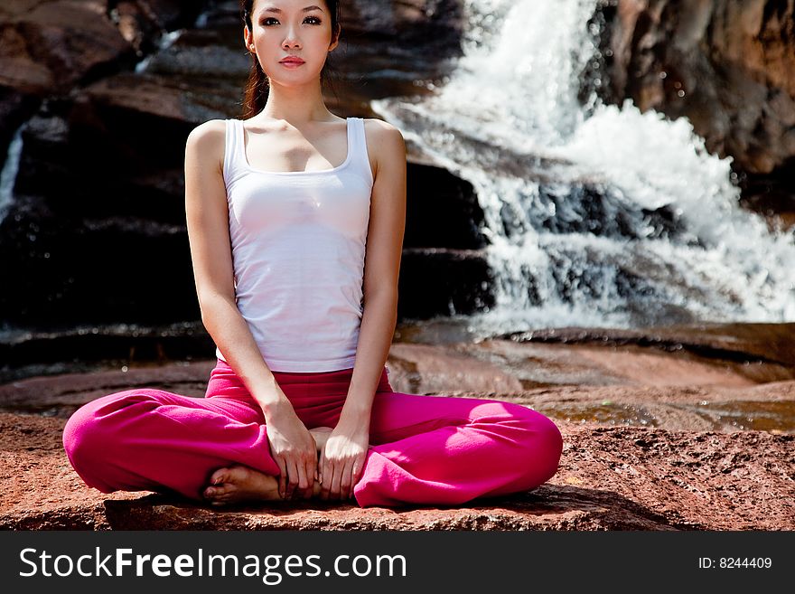 Outdoor young woman sitting by the waterfall meditating. Outdoor young woman sitting by the waterfall meditating