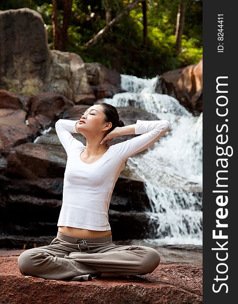 Outdoor young woman sitting by the waterfall meditating. Outdoor young woman sitting by the waterfall meditating