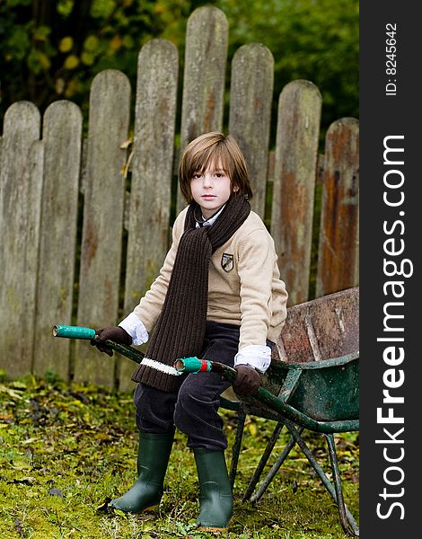 Closeup cute young boy sitting on a wheelbarrow in garden. Closeup cute young boy sitting on a wheelbarrow in garden