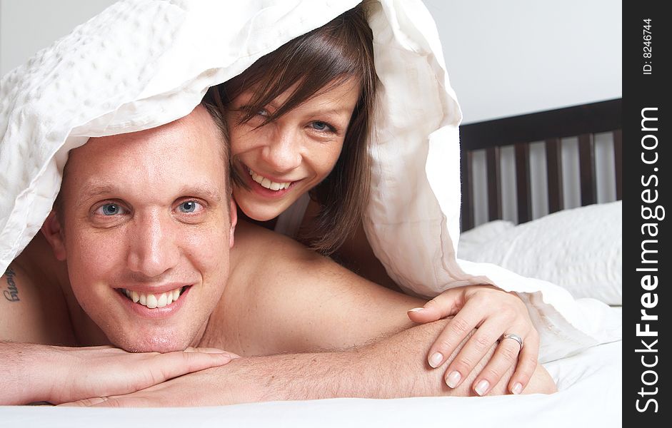 Young couple in their bed. They are playing in romance under the sheets. Young couple in their bed. They are playing in romance under the sheets.