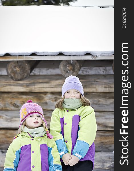 Two little girls standing in front of a log cabin at wintertime. Two little girls standing in front of a log cabin at wintertime.