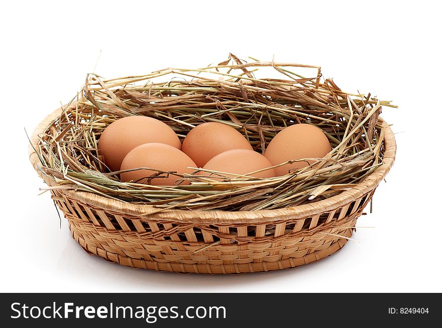 Chicken eggs and hay in  the brown basket .