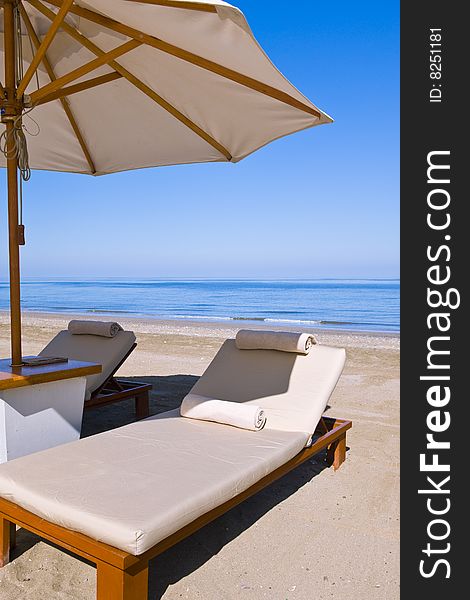 Idyllic scene of deck chairs under an umbrella on a clean beach in the hot afternoon sun. Idyllic scene of deck chairs under an umbrella on a clean beach in the hot afternoon sun.