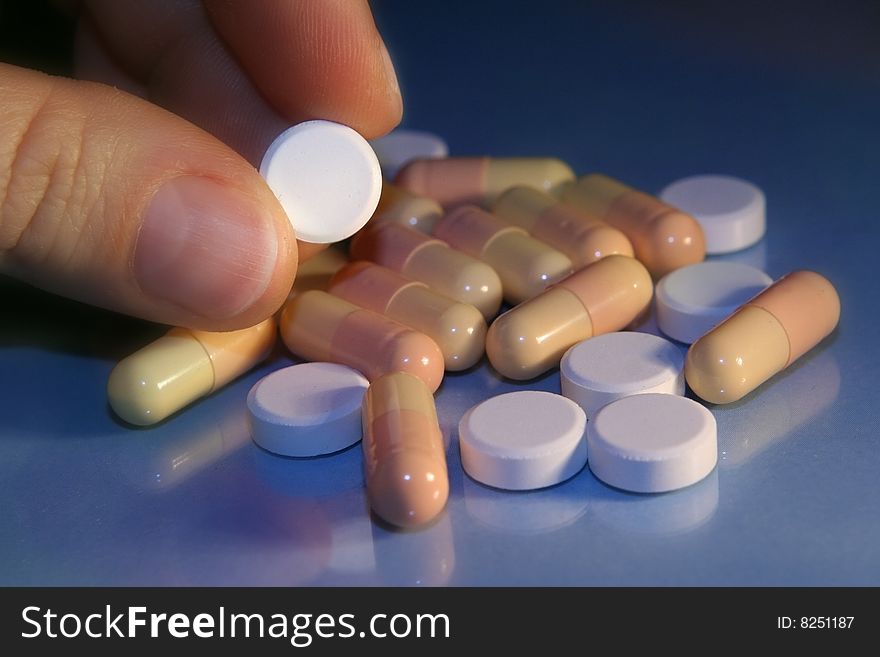 Round pills over blue background, one pill in fingers. Round pills over blue background, one pill in fingers