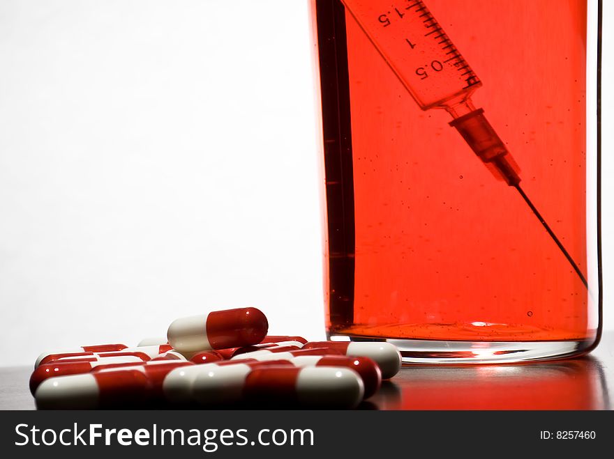 Tablets, a syringe into a glass with blood on a white background