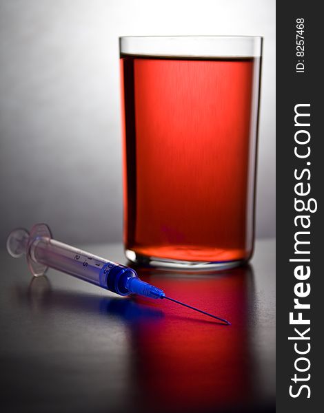 Syringe into a glass with blood  on a gray background