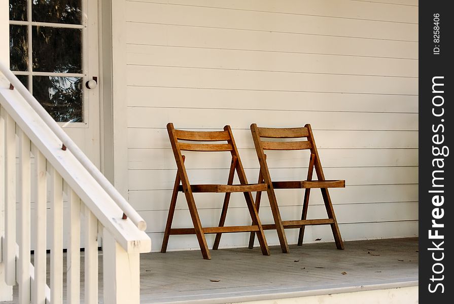 Two brown fold out chairs side by side on a porch. Two brown fold out chairs side by side on a porch.