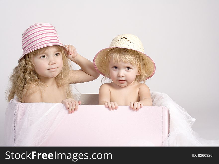 Two pretty sisters of 2 and 4 years old in summer bonnets sitting in big pink box