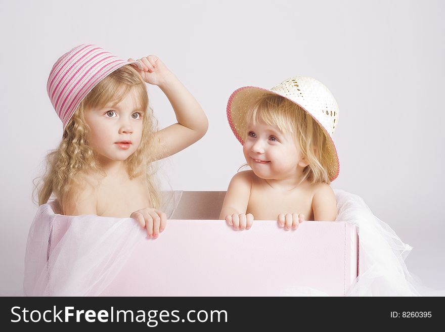 Two pretty sisters of 2 and 4 years old in summer bonnets sitting in big pink box