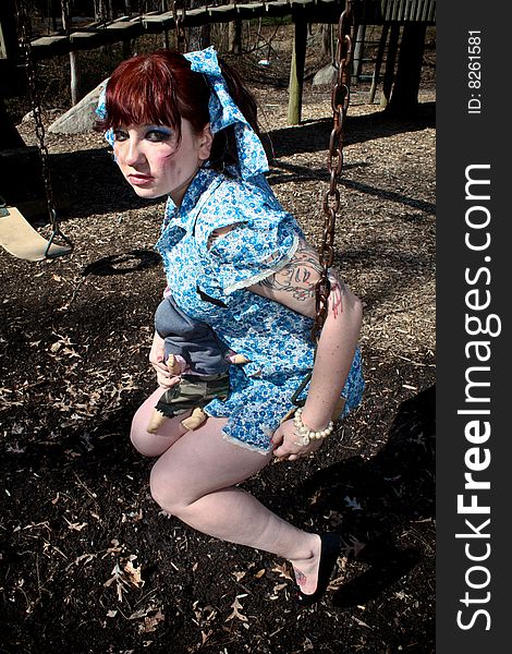 A girl sitting on a swing at the playground and holding a doll. A girl sitting on a swing at the playground and holding a doll