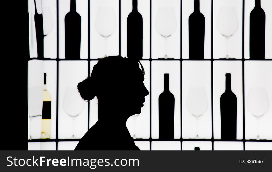 Silouette of a waitress against bottle and glasses on a luminous wall