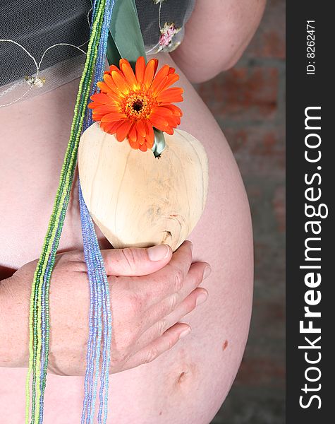 Heavily pregnant lady holding flower and wooden heart on her tummy. Heavily pregnant lady holding flower and wooden heart on her tummy