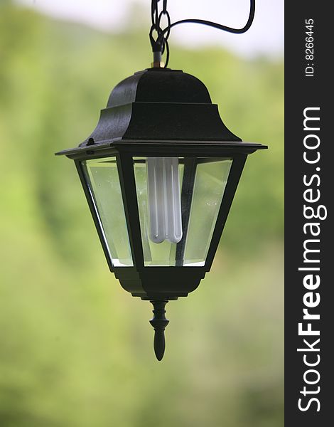 There is an electric street black lantern. There is a modern economical lamp inside it.