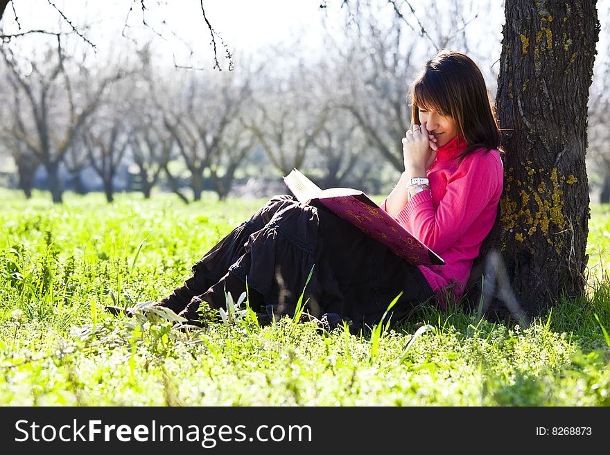 Young cheerful woman enjoying a book in the forest.