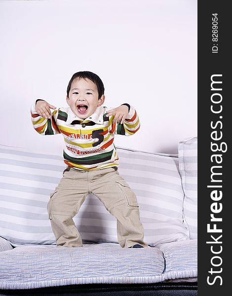A picture of a little chinese boy playing roles and having great fun on sofa at home