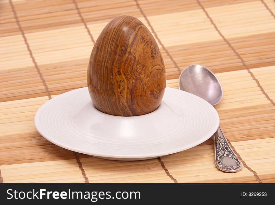 Served stone egg in a rest under egg with spoon. Close-up.