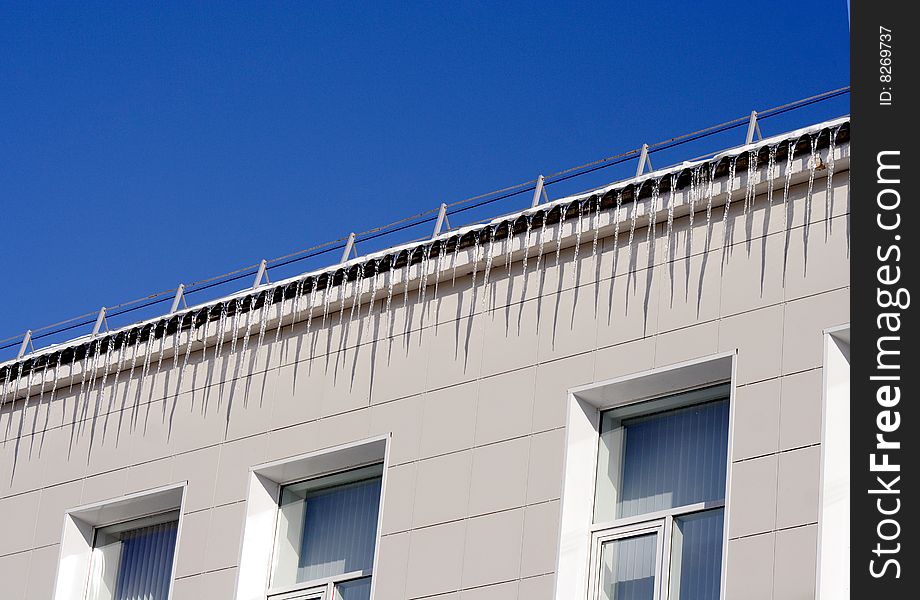 Long icicles winding from a roof buildings and blue sky. Long icicles winding from a roof buildings and blue sky