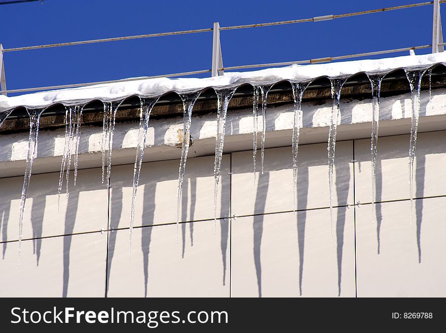 Long icicles winding from a roof buildings and blue sky. Long icicles winding from a roof buildings and blue sky