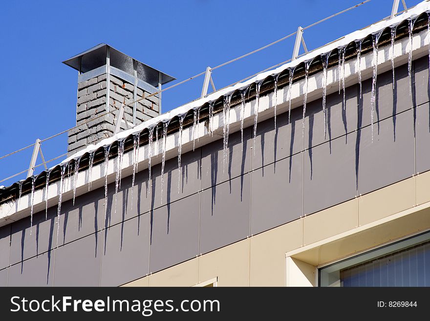 Long icicles winding from a roof buildings and blue sky. Long icicles winding from a roof buildings and blue sky