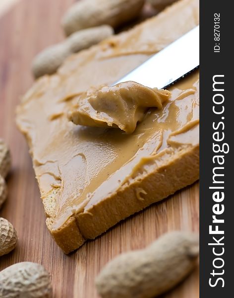 Slice of bread with peanut butter spread on wooden background.