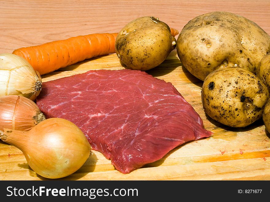 Onions, potatoes, carrots, meat on cutting board