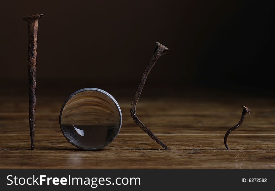 Three rusty nails and a lens on a wooden table. Three rusty nails and a lens on a wooden table
