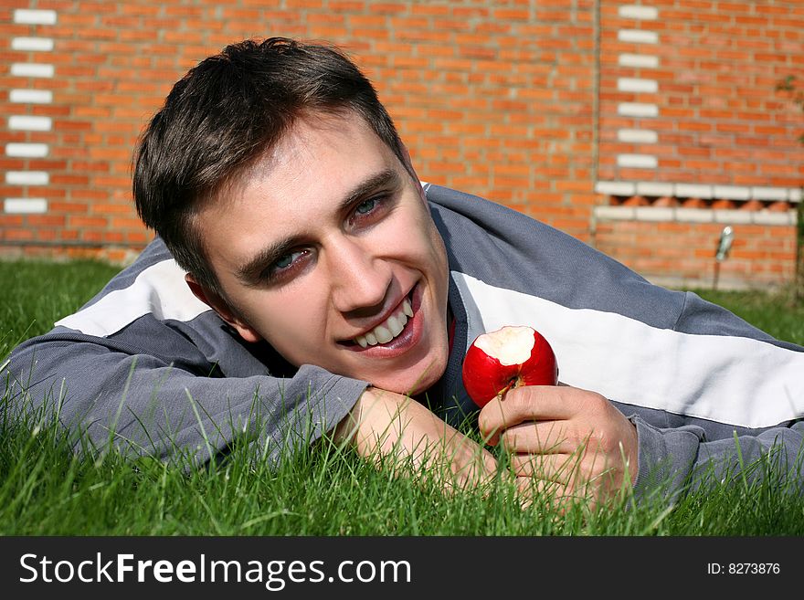 Young happy man with apple beside brick wall