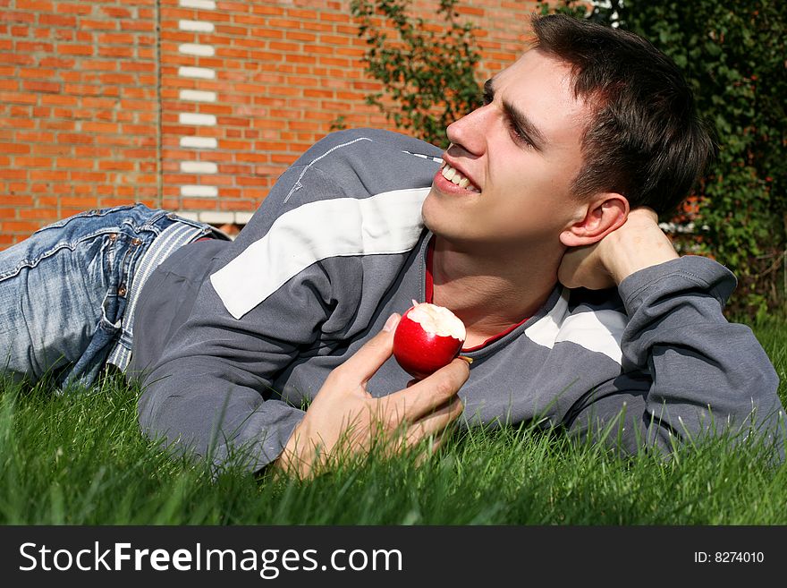 Young happy man with apple beside brick wall. Young happy man with apple beside brick wall