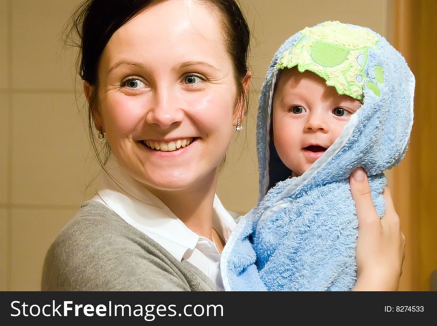 Portrait of happy young smiling mother holding her baby wrapped in a blue towel after his bath. Portrait of happy young smiling mother holding her baby wrapped in a blue towel after his bath.