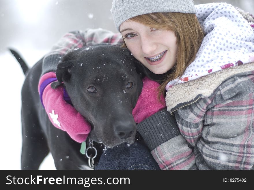 Teen girl sitting in snow with black lab dog. Teen girl sitting in snow with black lab dog