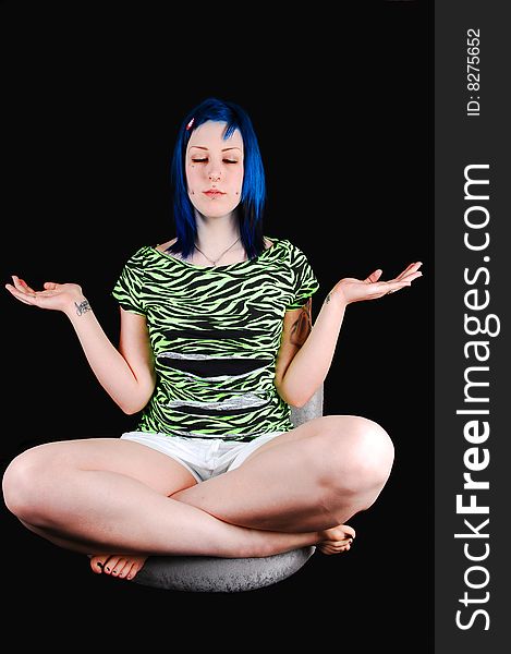 Pretty young blue haired girl is meditating in a green top and white 
shorts, sitting on a chair for black background. Pretty young blue haired girl is meditating in a green top and white 
shorts, sitting on a chair for black background.