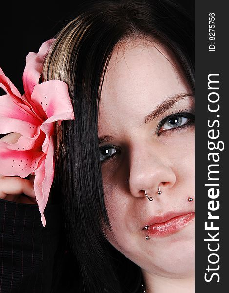 An pretty face shot with a pink flower and several piercing is looking in
the camera, on black background. An pretty face shot with a pink flower and several piercing is looking in
the camera, on black background.