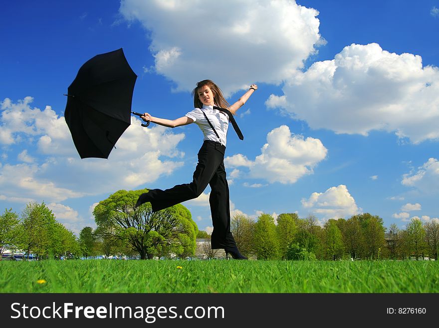 Business woman jumping on the field with umbrella