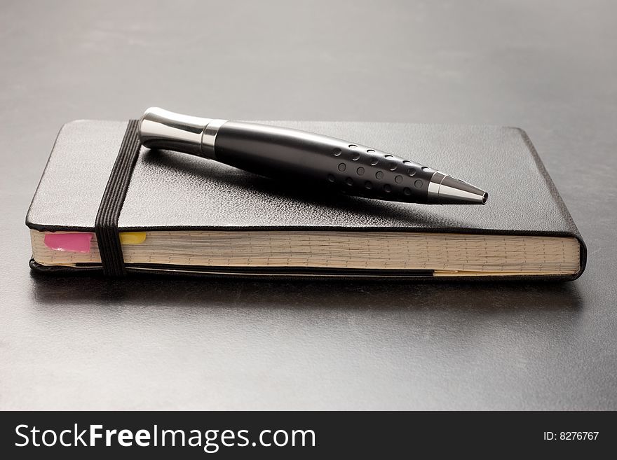 Black leather bound notebook on table with black shiny pen. Black leather bound notebook on table with black shiny pen.