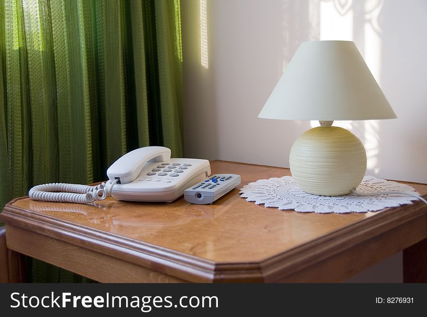 Corner of the room with phone, lamp and TV remote controller on table