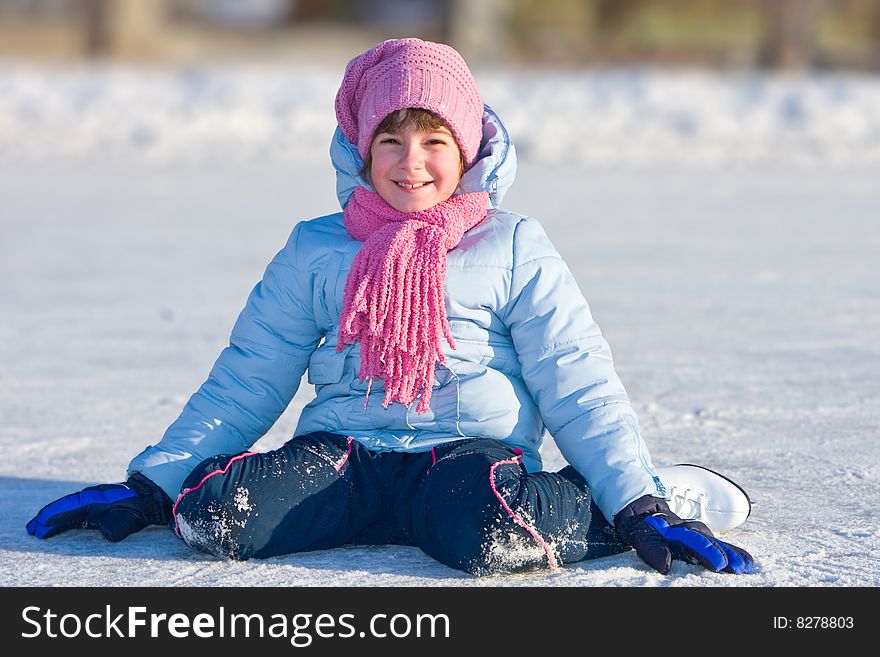 Girl on skates sitting on the ice.