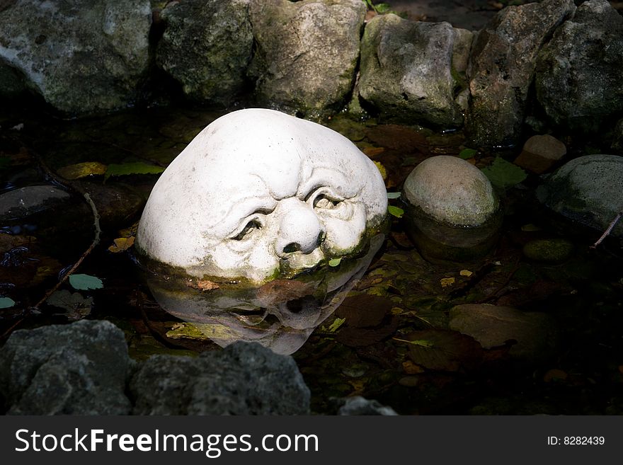 A sunlit decorative stone with carved face in a small pond. A sunlit decorative stone with carved face in a small pond