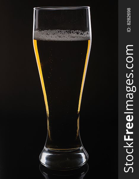 A glass of light beer on black background, lighted from behind. A glass of light beer on black background, lighted from behind